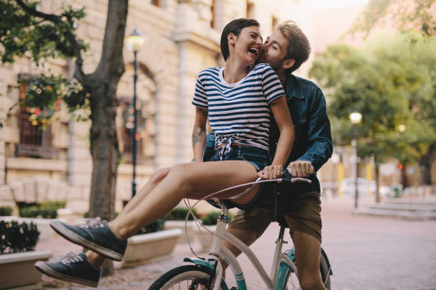 Couple having fun on a bicycle Laughing woman sitting on boyfriends bicycle handlebar. Cheerful couple on a bike together in the city having fun. boyfriend stock pictures, royalty-free photos & images
