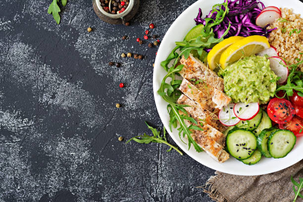 istock Healthy dinner. Buddha bowl lunch with grilled chicken and quinoa, tomato, guacamole, red cabbage, cucumber and arugula on gray background. Flat lay. Top view 961730574