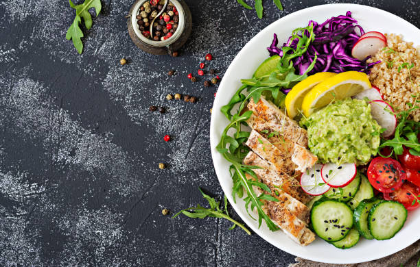 istock Healthy dinner. Buddha bowl lunch with grilled chicken and quinoa, tomato, guacamole, red cabbage, cucumber and arugula on gray background. Flat lay. Top view 961730596