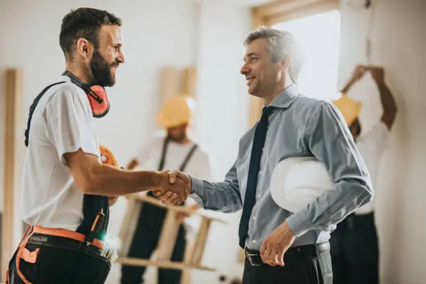 Happy construction worker greeting mid adult foreman at renovating apartment.