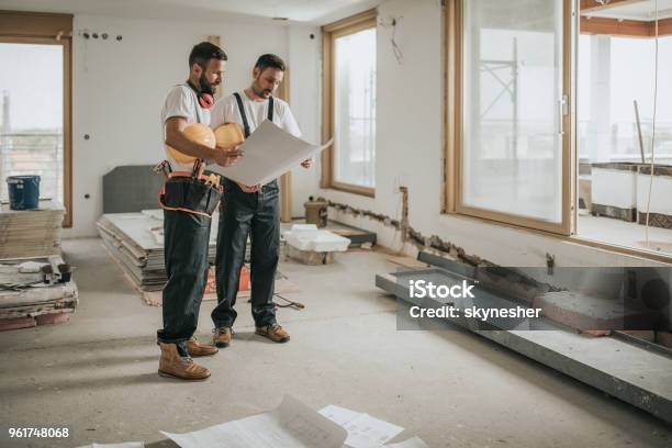Full Length Of Construction Workers Analyzing Blueprints In The Apartment Stock Photo - Download Image Now