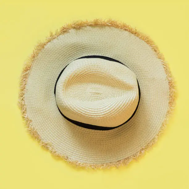 Straw beach sun-hat on yellow. Female outfit for heat. Square image. Minimal summer.