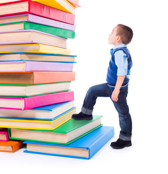 Little boy looking up to stacked big books stock photo