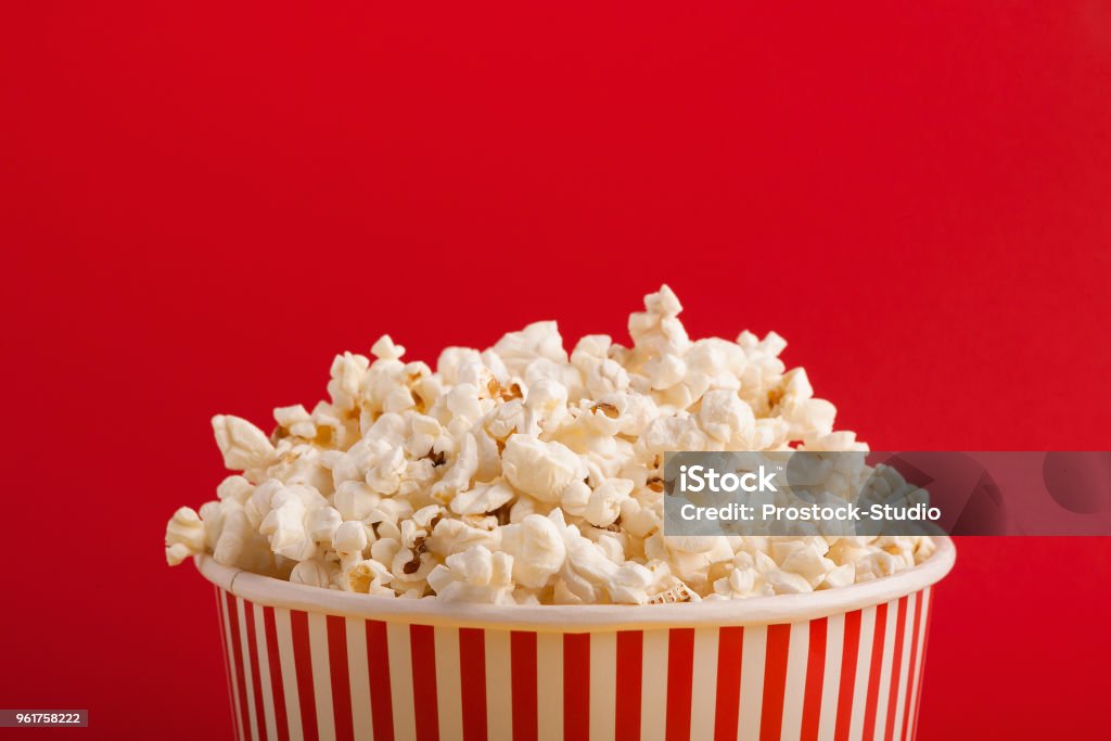 Bucket of popcorn on red background Popcorn in classic striped bukcet on red background. Fluffy maise paper box, copy space. Fast food and movie snack, entertainment concept Popcorn Stock Photo