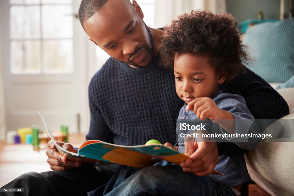 Father And Young Son Reading Book Together At Home Family Stock Photo