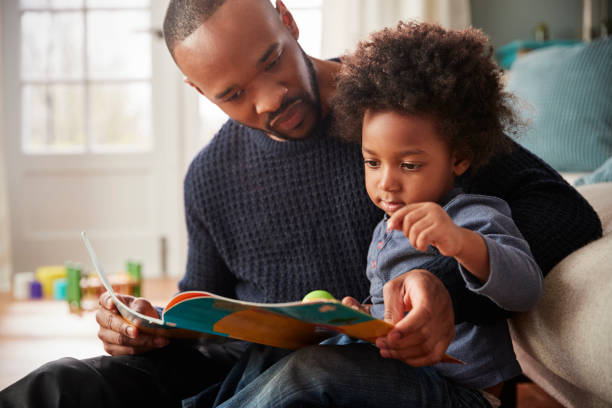 отец и маленький сын читают книгу вместе дома - family reading book child стоковые фото и изображения