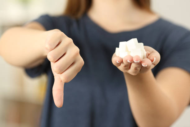 Woman hand holding sugar cubes with thumbs down Front view close up of a woman hand holding sugar cubes with thumbs down at home infamous stock pictures, royalty-free photos & images