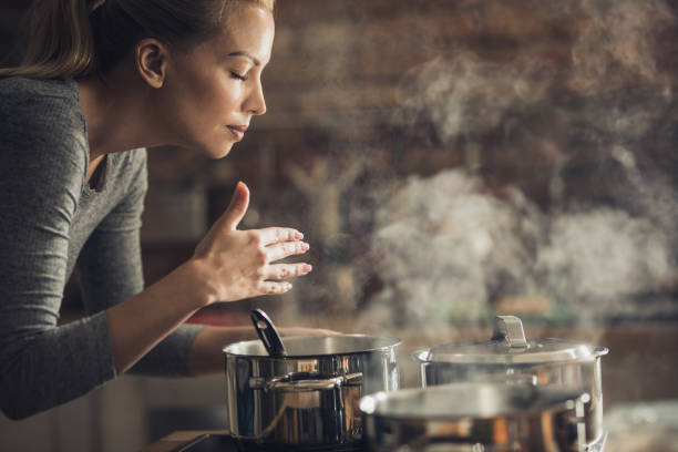 hermosa mujer que huele delicioso almuerzo está preparando en la cocina. - oliendo fotografías e imágenes de stock