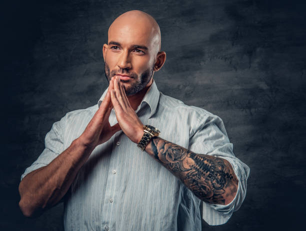 istock Praying shaved head man with tattoos on his arm. 961782930