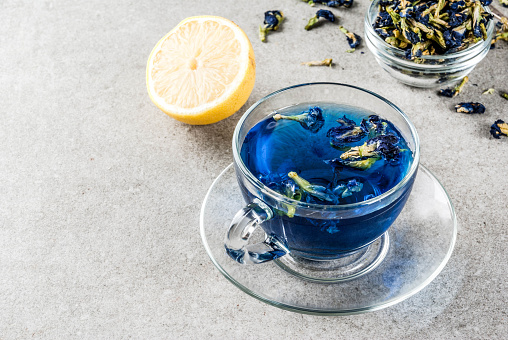 Healthy drinks, organic blue butterfly pea flower tea with limes and lemons, grey concrete background copy space