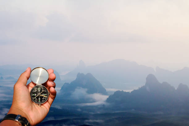 istock Man hand with a black and silver compass in green mountain blur. 961789698