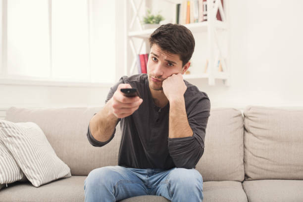 istock Young boring man watching television at home 961789916