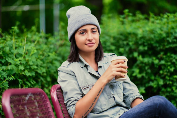 istock Brunette female in a hat drinks coffee in a summer park. 961789934