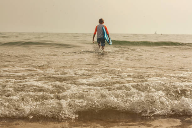 Rear view kid surfing with a board in the beach stock photo