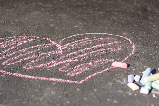 Chalk drawn pink heart on dark grey asphalt