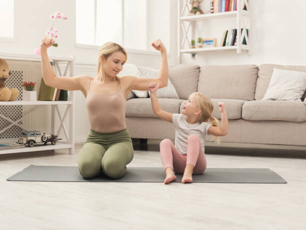 Mother and little daughter doing yoga together Beautiful mother and charming little daughter practicing yoga together at home, showing physical strength with muscular hands, copy space blonde female bodybuilders stock pictures, royalty-free photos & images