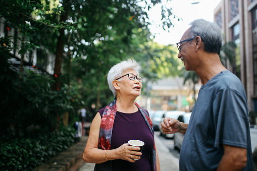 Older senior man and woman standing on the street of Kuala Lumpur, talking. They could be friends that haven’t seen each other in a while, or just neighbors talking everyday things.