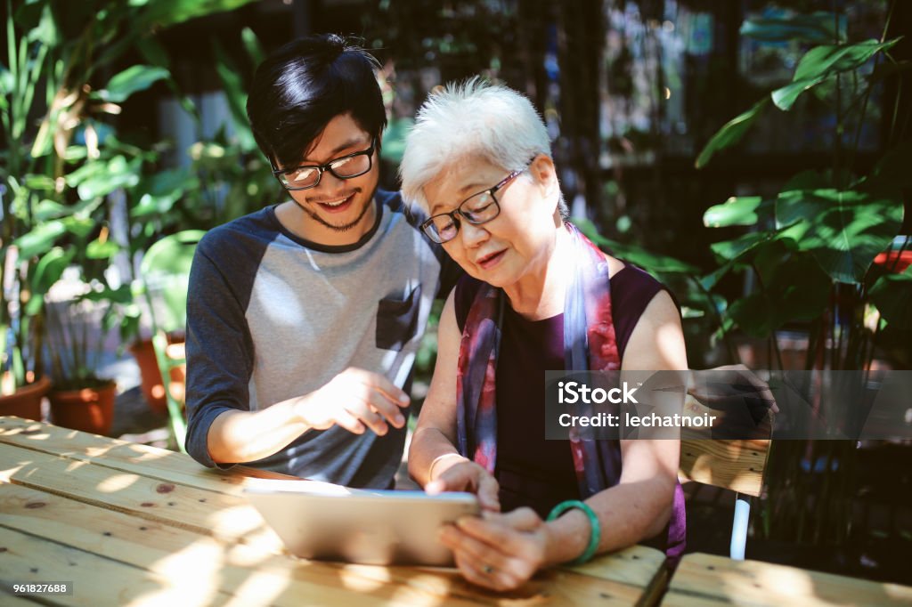 Senior woman looking at the digital tablet, receiving instructions from grandson Young man is showing his grandmother modern things on a digital tablet. Millennials vs seniors, senior woman is receiving help on how to use modern technologies. Asia Stock Photo