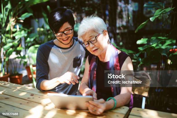 Senior Woman Looking At The Digital Tablet Receiving Instructions From Grandson Stock Photo - Download Image Now