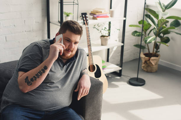 istock overweight man talking by smartphone on sofa at home 961829628