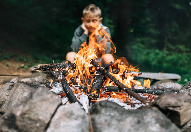 istock Boy sits near campfire in forest 961829922