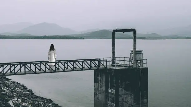 Photo of woman standing at water level gate, horror scene in white tone9