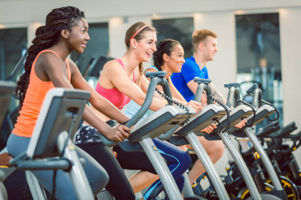 Side view of a beautiful woman smiling while cycling during exercising class at the gym brunette beautiful woman smiling while cycling on a modern fitness bicycle during group exercising class at the gym exercise bike stock pictures, royalty-free photos & images