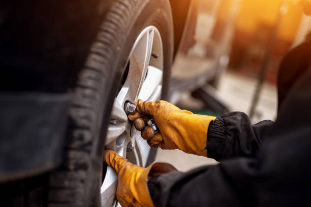 istock Auto mechanic man with electric screwdriver changing tire outside. Car service. Hands replace tires on wheels. Tire installation concept. 961837954