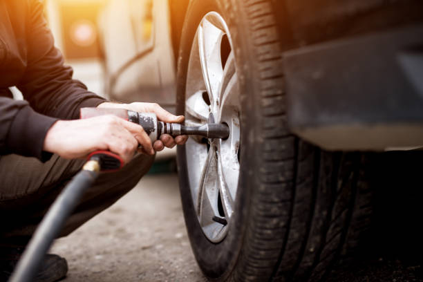 istock Auto mechanic man with electric screwdriver changing tire outside. Car service. Hands replace tires on wheels. Tire installation concept. 961841280