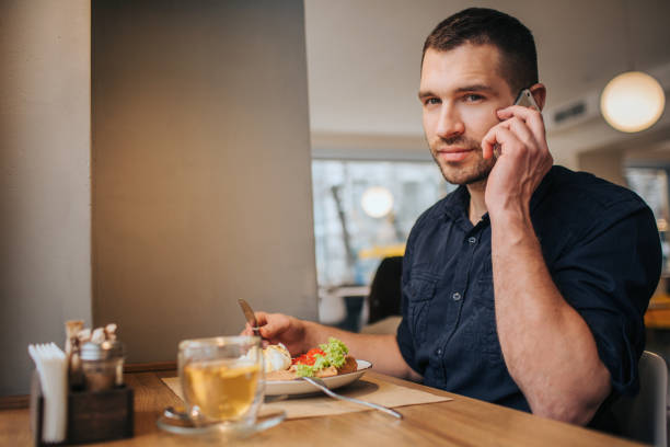istock Guy is sitting in cafe and having dinner. Also he is talking on the phone and looking straight to camera. He looks good and confident 961842538