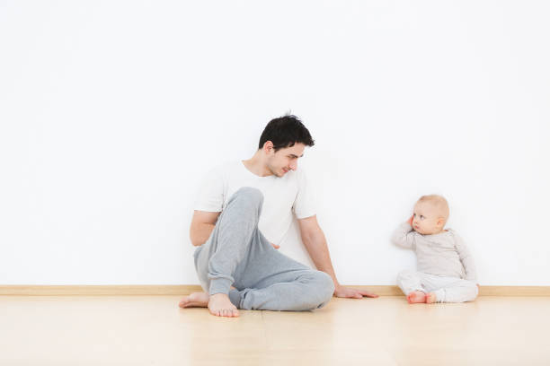 Mutual understanding between children and their parents. Young father tries to understand his little son. Lifestyle family portrait on white wall background at home. Copy space