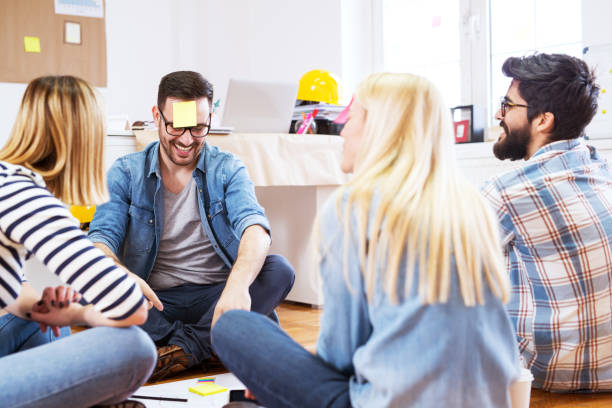 istock Young playful happy group of people sitting on office floor while playing guess the note. 961850344