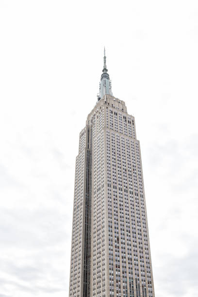 nahaufnahme der spitze des empire state building isoliert gegen weiße wolkenhimmel während tag auf dem dach berühmten beeindruckendes gebäude in new york herald square midtown, hohen hohen turm - chrysler stock-fotos und bilder