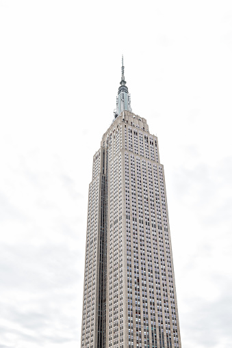 New York City, USA - April 7, 2018: Closeup of top of empire state building isolated against cloudy white sky during day rooftop famous iconic building in NYC Herald Square Midtown, high tall spire