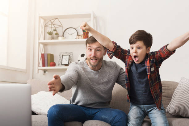 padre e figlio guardano il calcio in tv a casa - family television watching watching tv foto e immagini stock