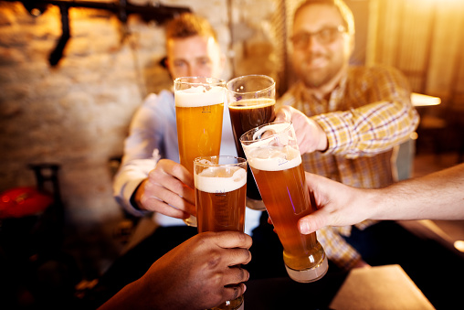 A group of young men clinking glasses with a beer in the sunny pub.