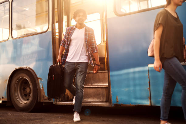istock Young handsome man is leaving the bus with his traveling bag. 961885458