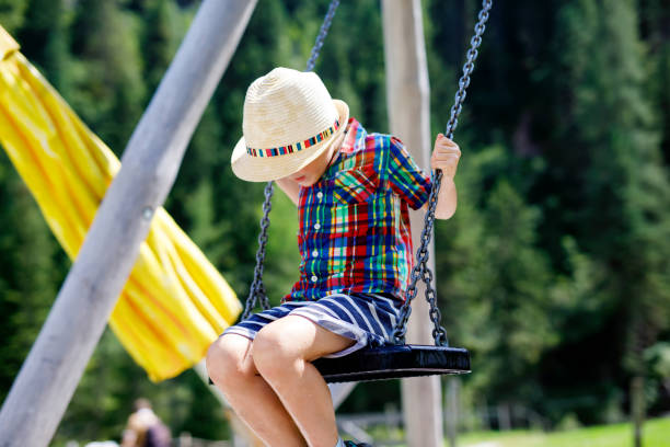 istock Funny kid boy having fun with chain swing on outdoor playground while being wet splashed with water 961885536