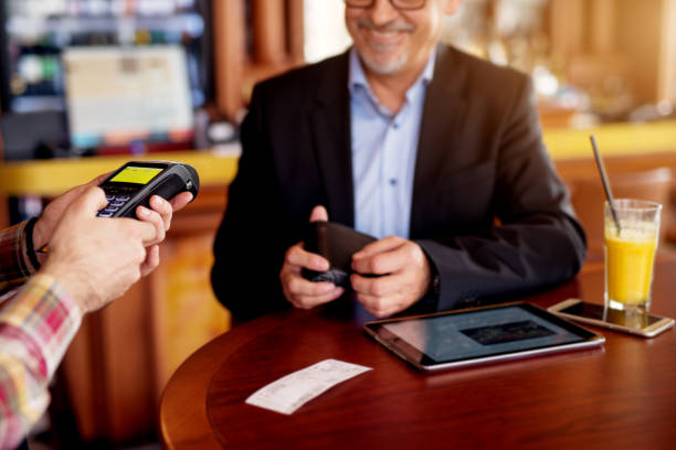 istock Mature cheerful businessman is using a tablet and paying check with the credit card while sitting in a coffee shop. 961888254