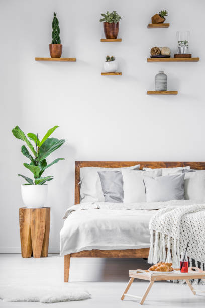 istock Breakfast tray standing on the floor beside a big comfortable bed with linen, blanket and pillows in a white bedroom interior. Real photo. 961902700