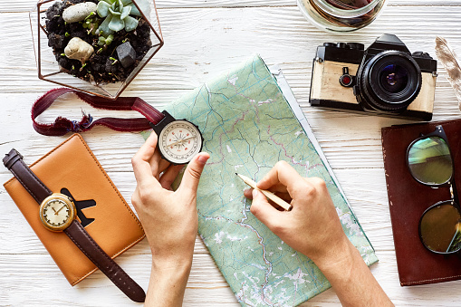 wanderlust and travel concept flat lay. hand holding compass and pencil on map exploring. passport money glasses photo camera on white wooden background. planning vacation. space for text