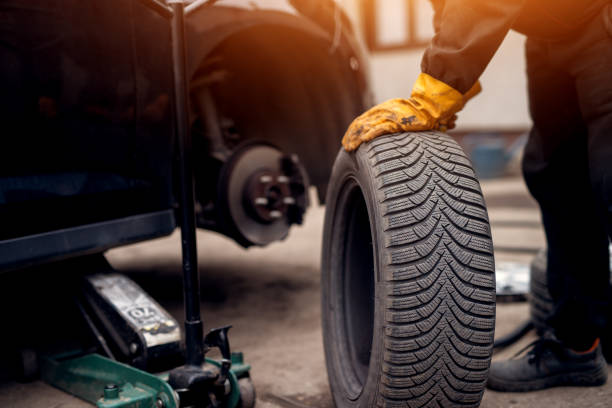 istock Auto mechanic man with electric screwdriver changing tire outside. Car service. Hands replace tires on wheels. Tire installation concept. 961905210