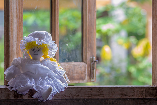 Doll girl sitting by the window alone .