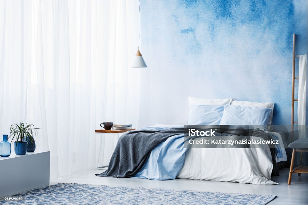 Plant on white cupboard in spacious blue bedroom interior with grey blanket on bed Bedroom Stock Photo
