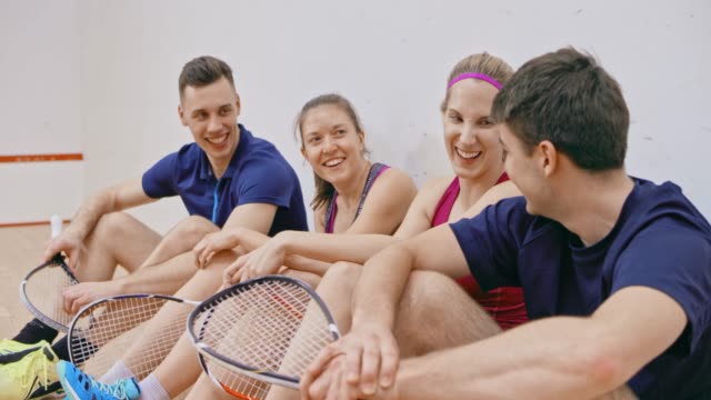 Four young adults sitting in the squash court and talking after the game