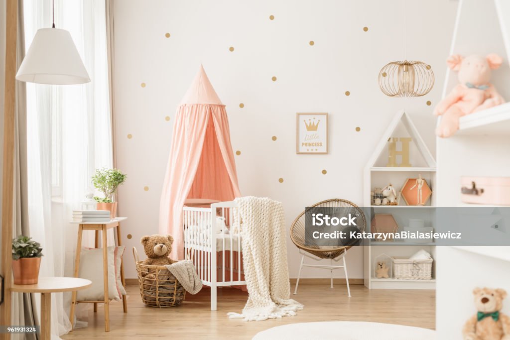 Gold and pink baby's bedroom Canopied cradle between gold armchair and basket with teddy bear in pink baby's bedroom interior Child Stock Photo