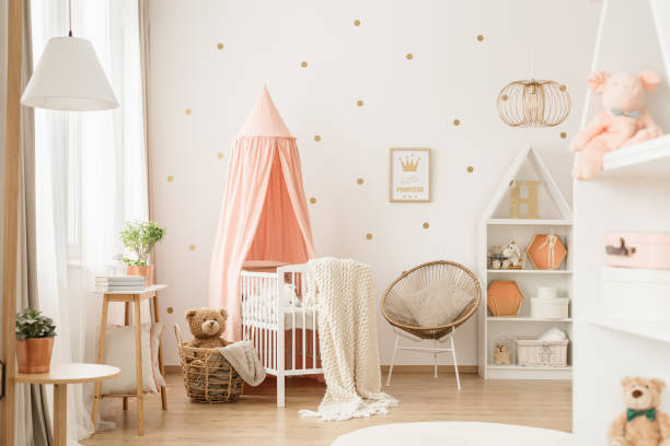 Gold and pink baby's bedroom Canopied cradle between gold armchair and basket with teddy bear in pink baby's bedroom interior bedroom stock pictures, royalty-free photos & images