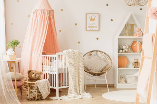 Pink child's bedroom interior Gold poster on the wall in child's bedroom interior with armchair next to pink cradle with knit blanket plush bear stock pictures, royalty-free photos & images