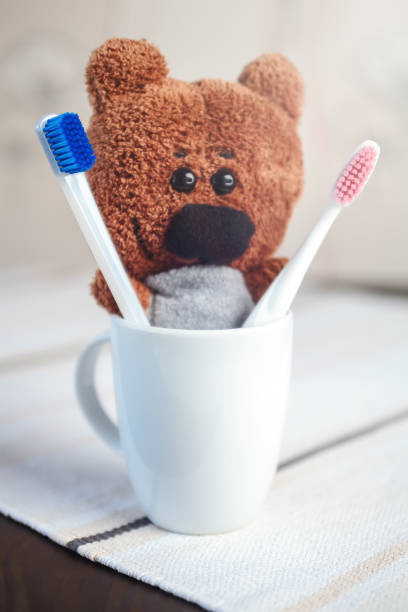 istock Handmade Teddy Bear with Red and Blue Plastic Toothbrushes in White Mug on Blurred Background Concept Dental 961946052