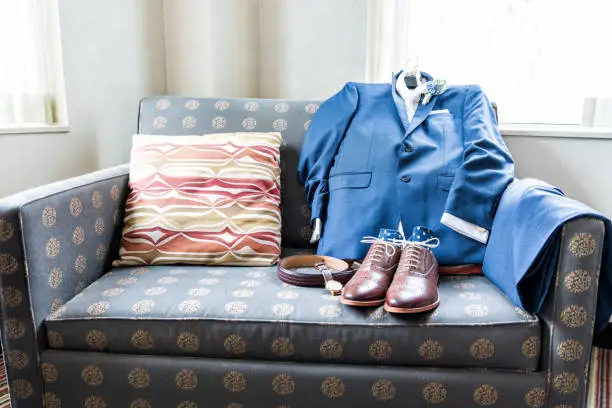 Men's leather new brown shoes closeup still life arrange on blue couch with socks, watch, suit for getting ready wedding preparation in room